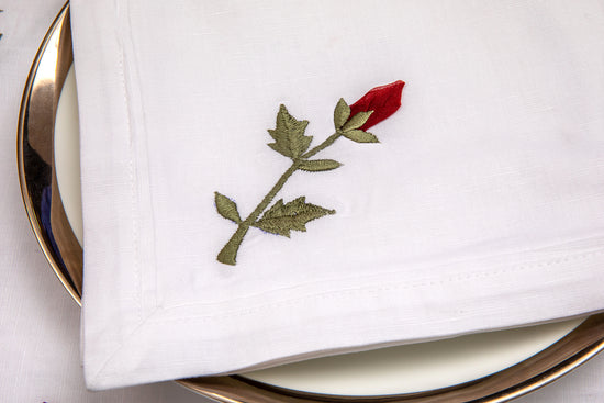 White linen dinner napkins with rosebud embroidery.