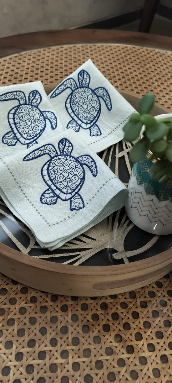 Powder blue linen cocktail napkin with embroidered turtle.