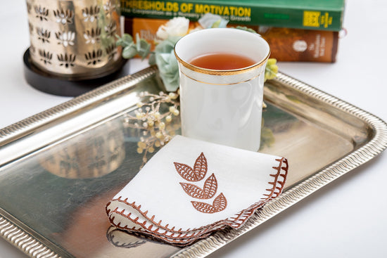 White linen cocktail napkin with brown leaf embroidery.