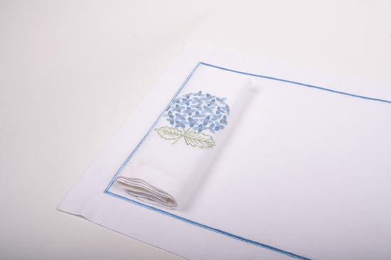 White linen placemats with blue embroidery and napkins with embroidered hydrangea.