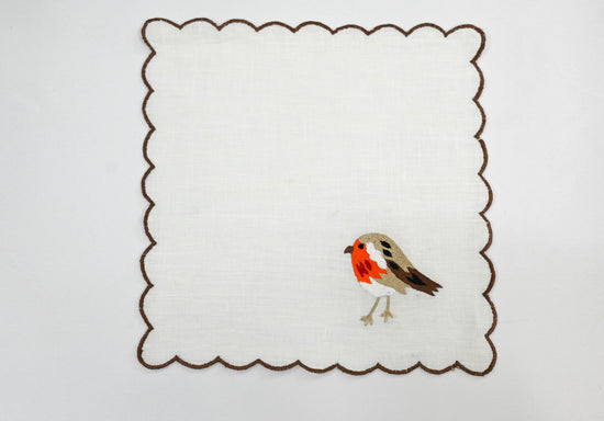 White linen cocktail napkin with orange brown bird embroidery.