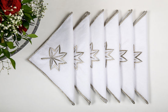 White linen dinner napkins embroidered in gold.