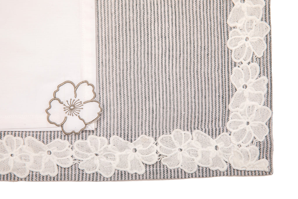 Laced striped placemats  and white linen dinner napkins with floral embroidery.
