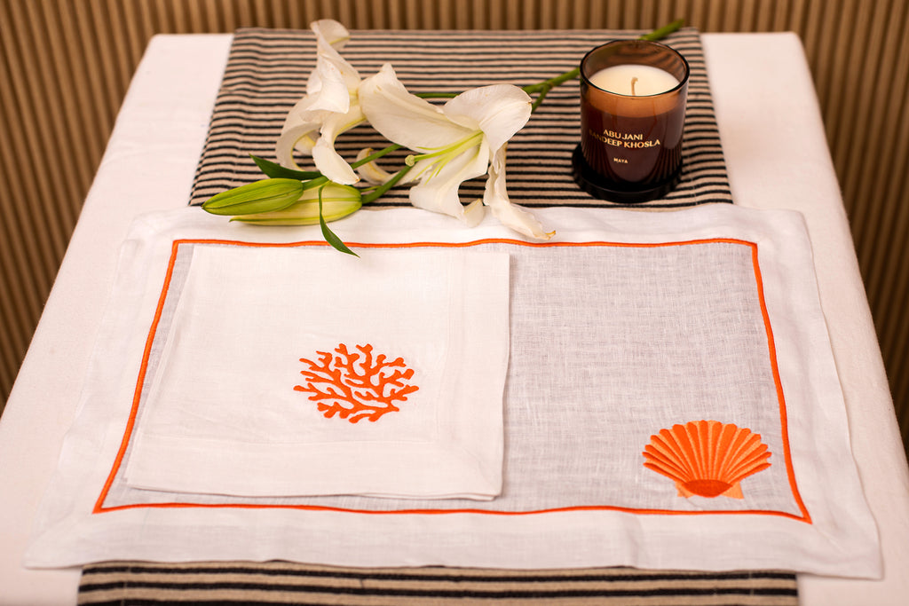 White linen placemat and napkin with striking shells and coral embroidery.