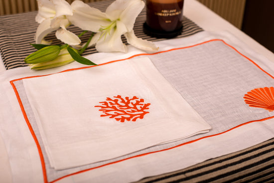 White linen placemat and napkin with striking shells and coral embroidery.