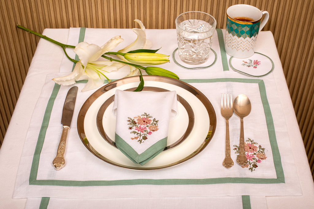 White linen embroidered placemat and napkin with mint green floral detailing.
