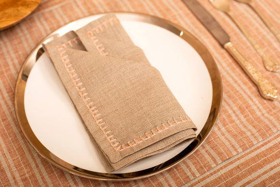 Rust and silver striped linen placemat and beige embroidered linen napkin.