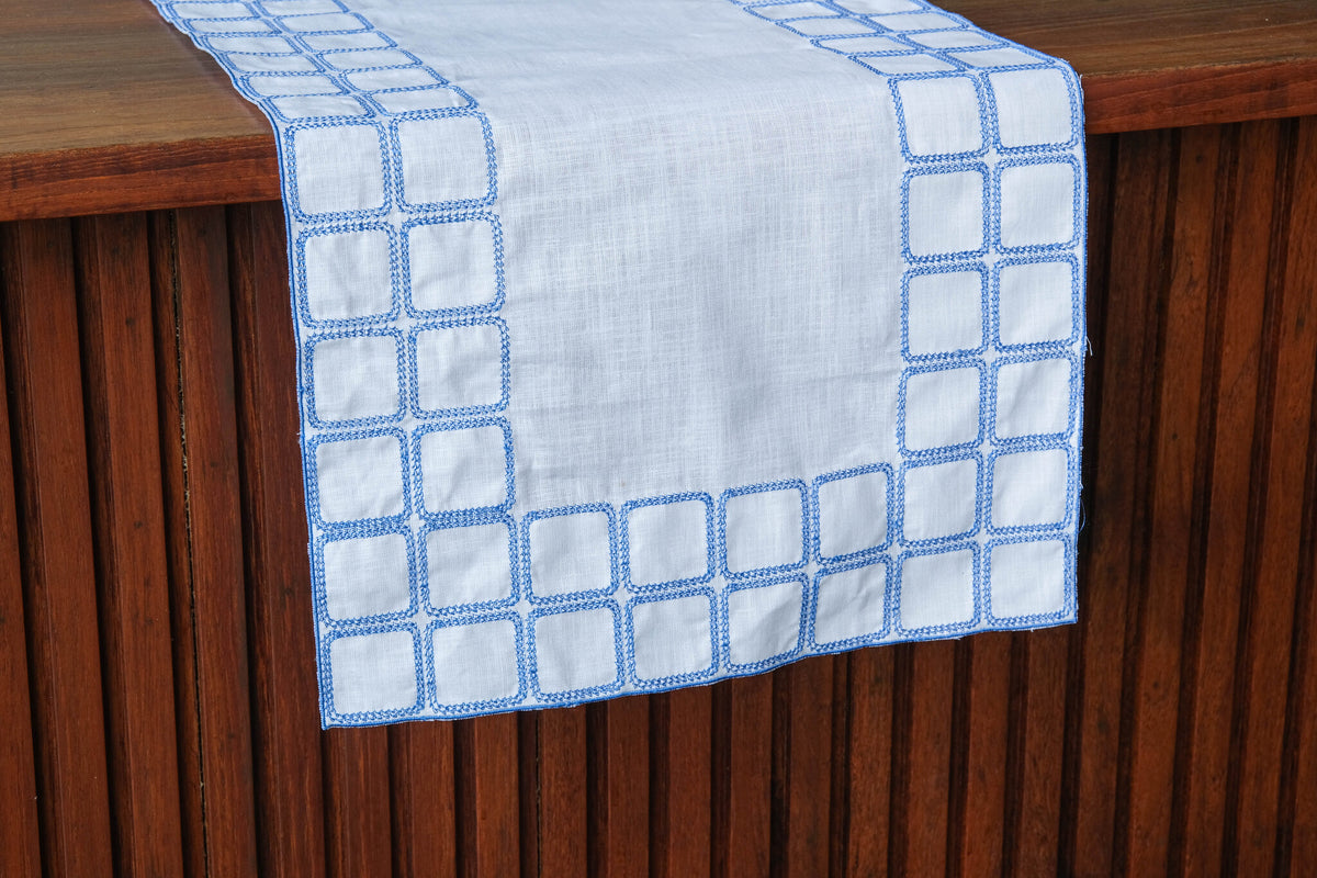 White linen runner with blue embroidery.