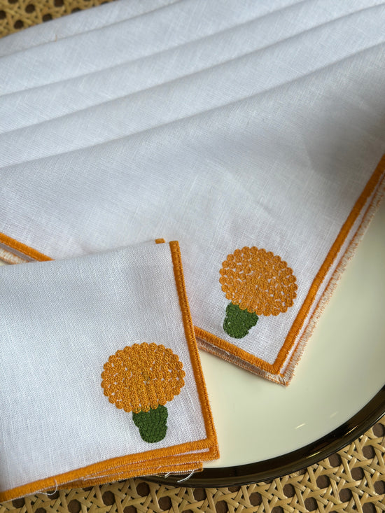 White linen cocktail napkins with  embroidered marigold.