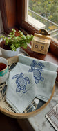 Powder blue linen cocktail napkin with embroidered turtle.