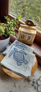 Powder blue linen cocktail napkin with embroidered turtle.