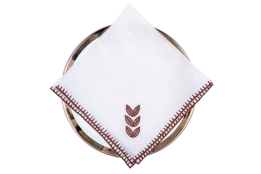 White linen dinner napkins with brown leaf embroidery.