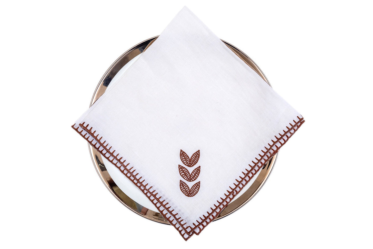 White linen dinner napkins with brown leaf embroidery.