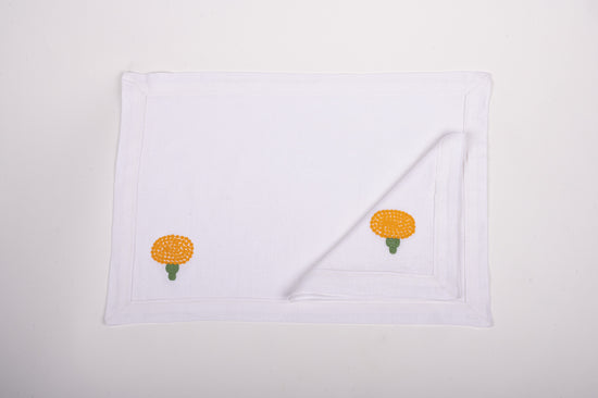 White linen placemats and napkins with marigold embroidery.