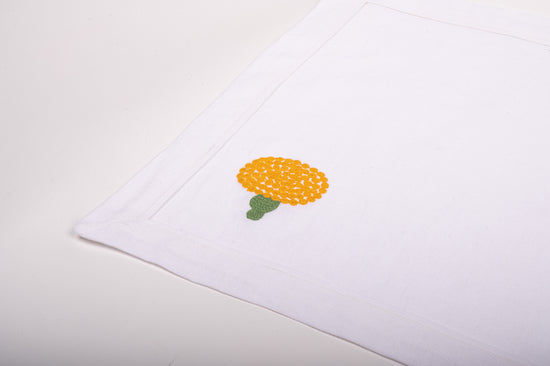 White linen placemats and napkins with marigold embroidery.