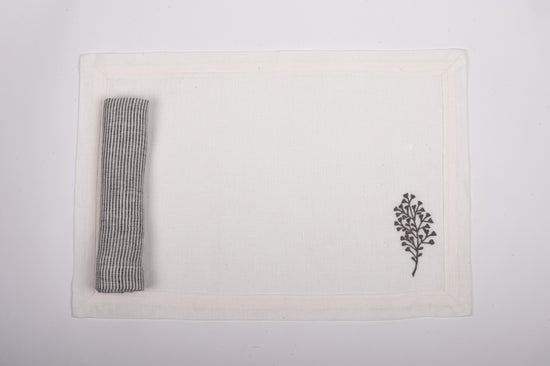 White linen placemats with fern embroidery and with black and white striped napkins.