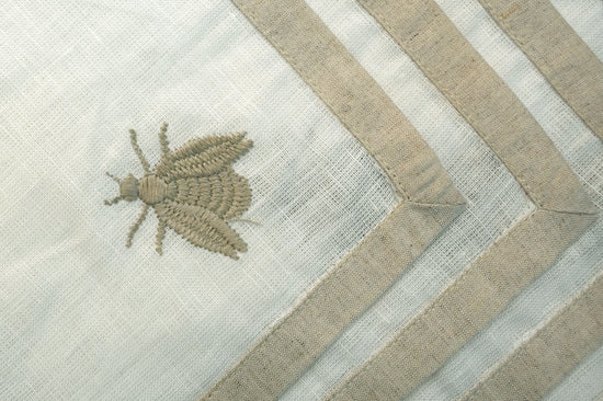 White linen cocktail napkins with a natural flange and embroidered beetle