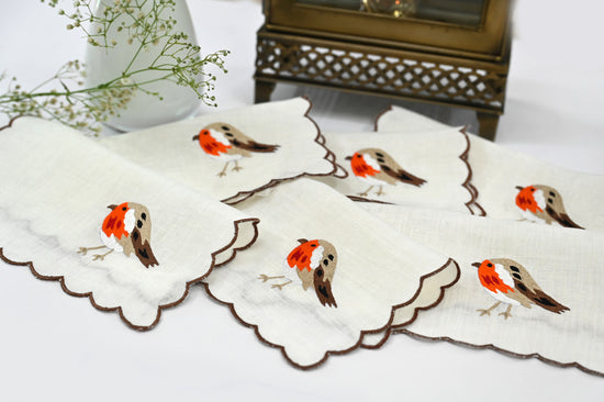 White linen cocktail napkin with orange brown bird embroidery.