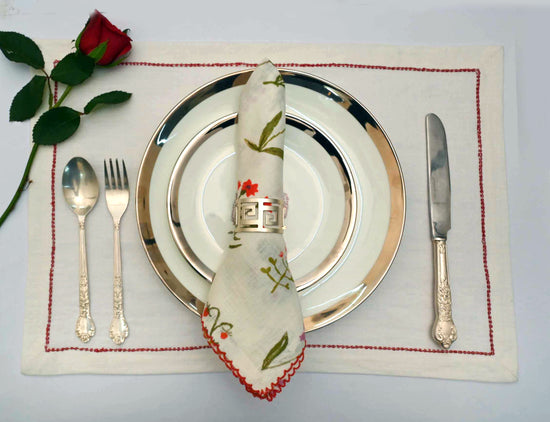 White linen placemats with red embroidery with printed linen embroidered napkins.