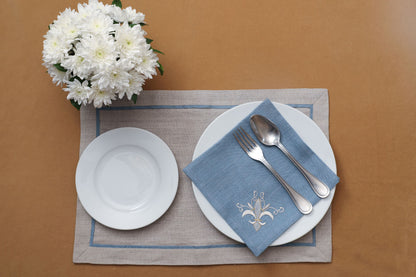 Blue linen napkins with regal motif and natural brown linen placemats with blue piping.