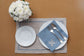 Blue linen napkins with regal motif and natural brown linen placemats with blue piping.