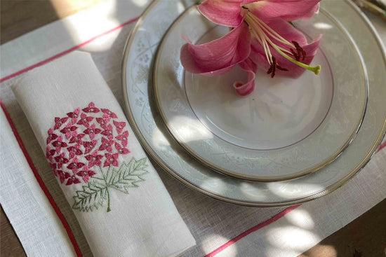 White linen placemats with pink embroidery and napkins with embroidered hydrangea.