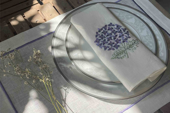 White linen placemats with purple embroidery and napkins with embroidered hydrangea.